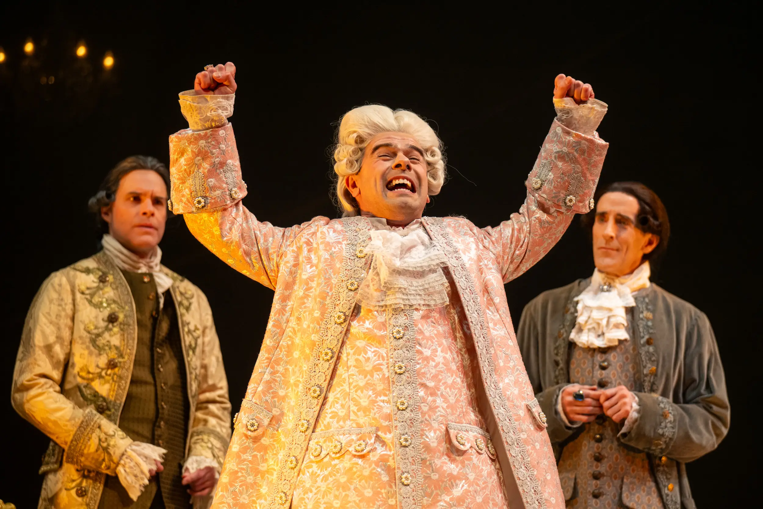 Man with white curled wig with his hands in the air, and two actors behind him as part of a performance.