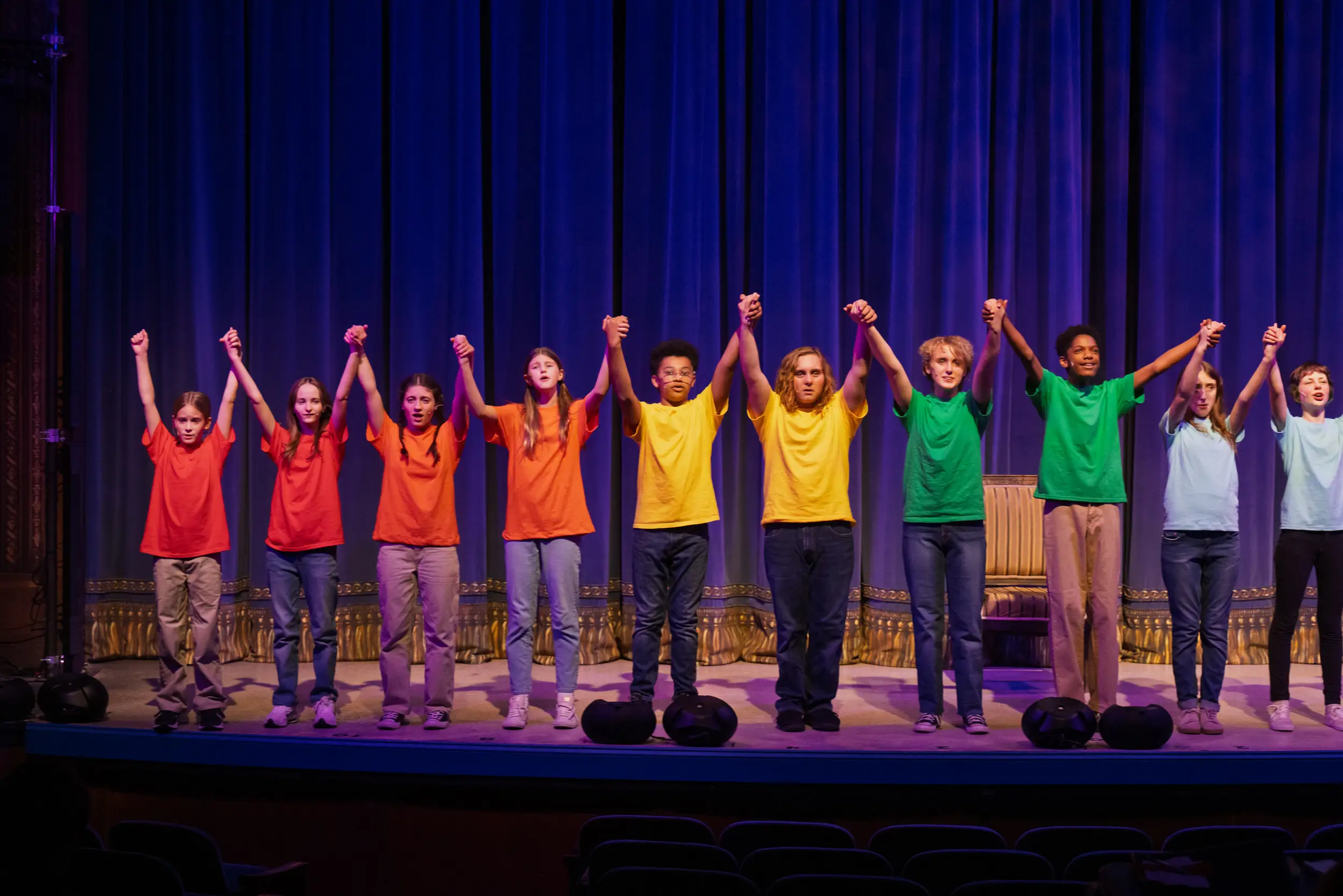 Kids on stage holding hands and raising them up at young performers performance.