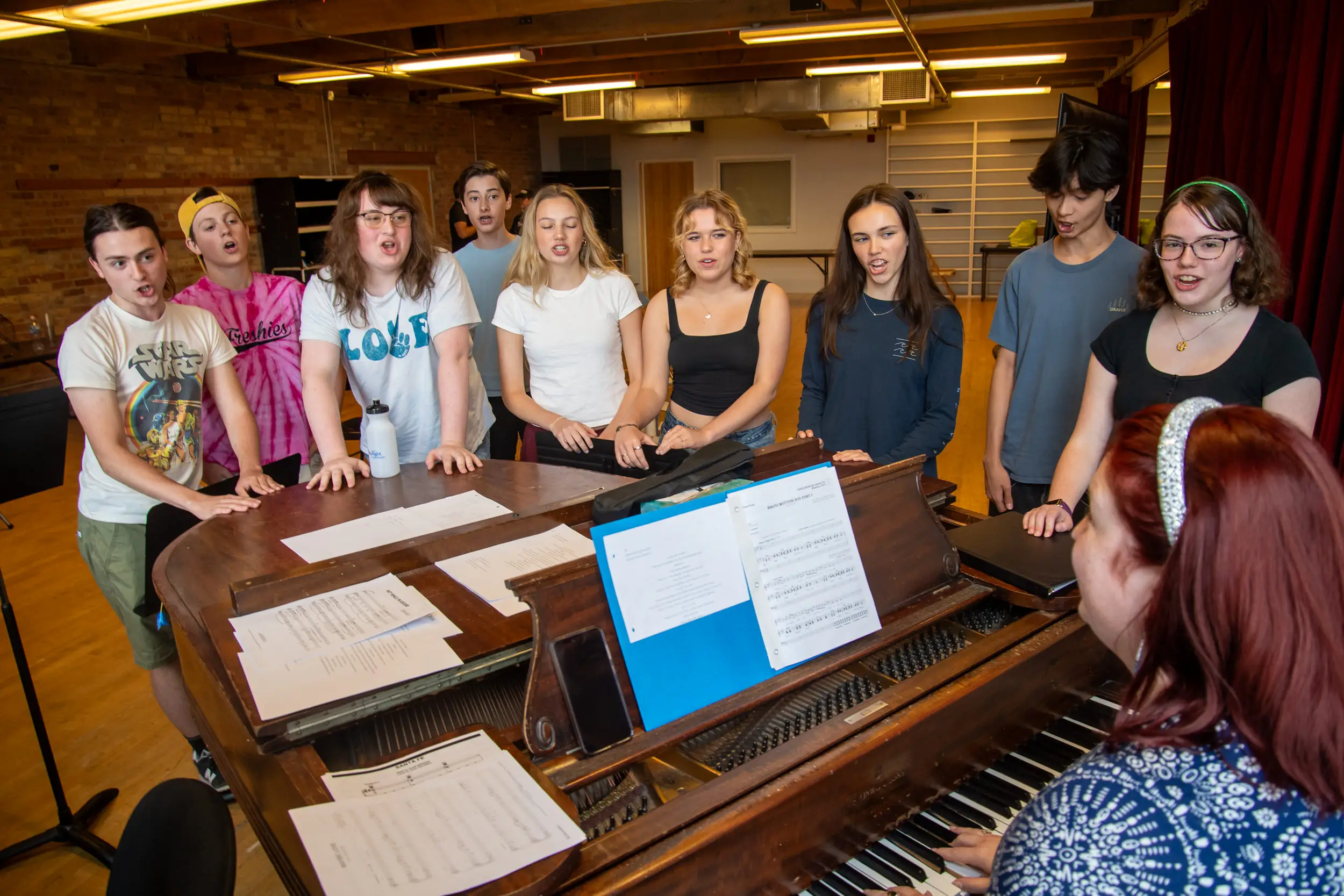 Woman playing piano with summer musical camp students around her.