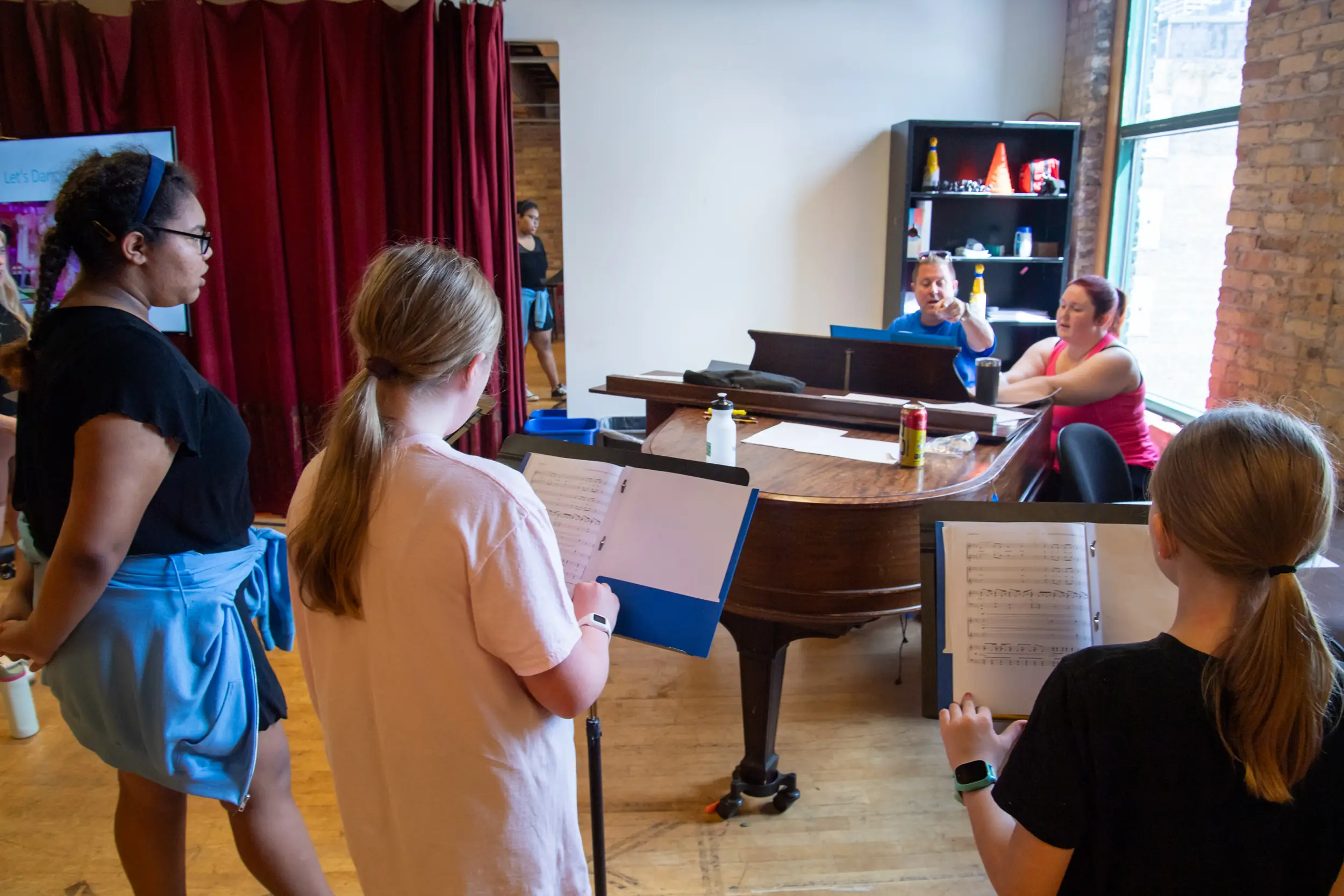 Man and woman at piano directing three kids to sing